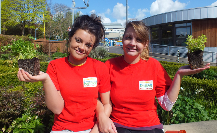 Two people in Post Code Lottery tee shirts holding plants