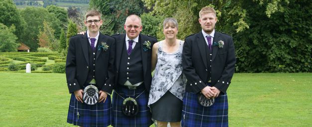 Davy, wearing kilt, with partner and sons standing for family photo