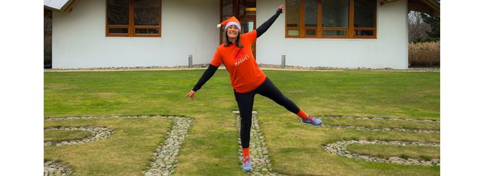 Woman in orange Maggie's T-shirt in star pose in front of Maggie's Dundee centre.