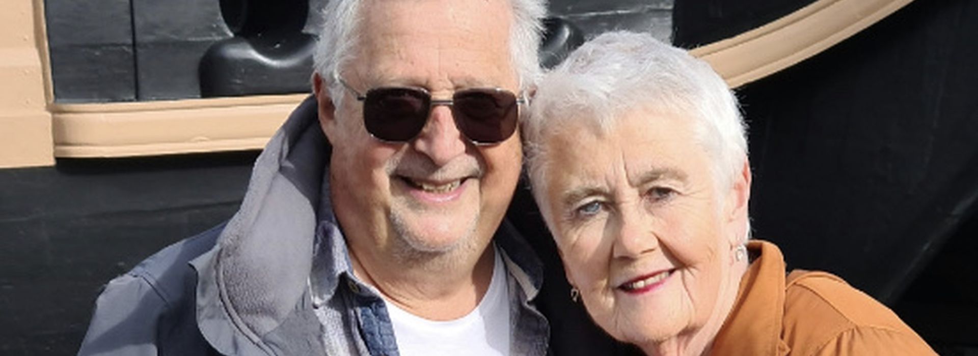 Marcus and wife Maggie standing together outside on sunny day day, smiling