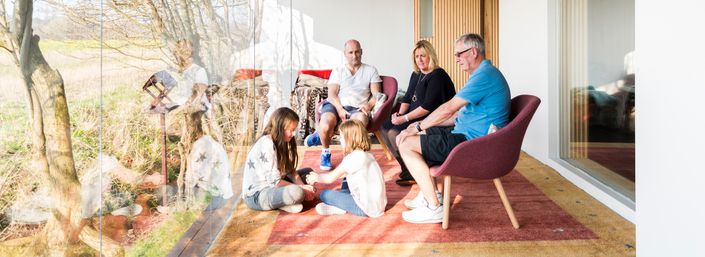 Two girls play sitting on rug, with adults talking with cancer support specialist behind them