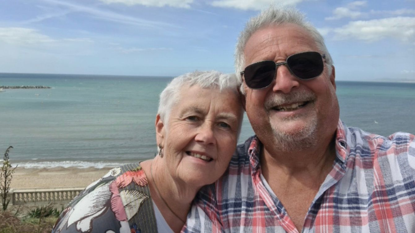 Marcus and his wife Maggie standing at the beach smiling at the camera