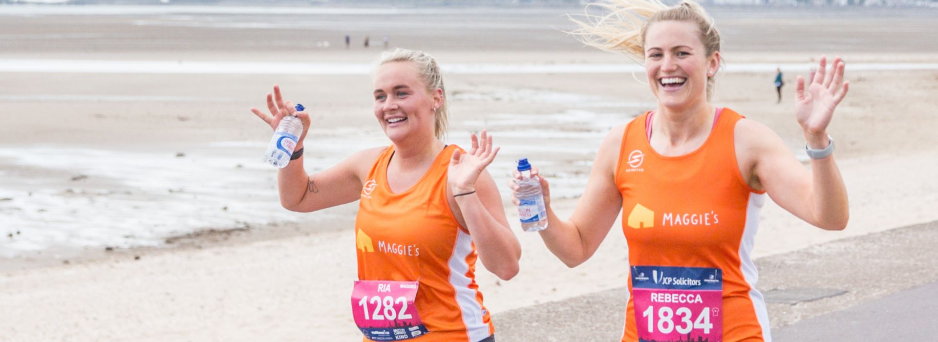 Two women, smiling, running the Swansea Half Marathon with beach in background