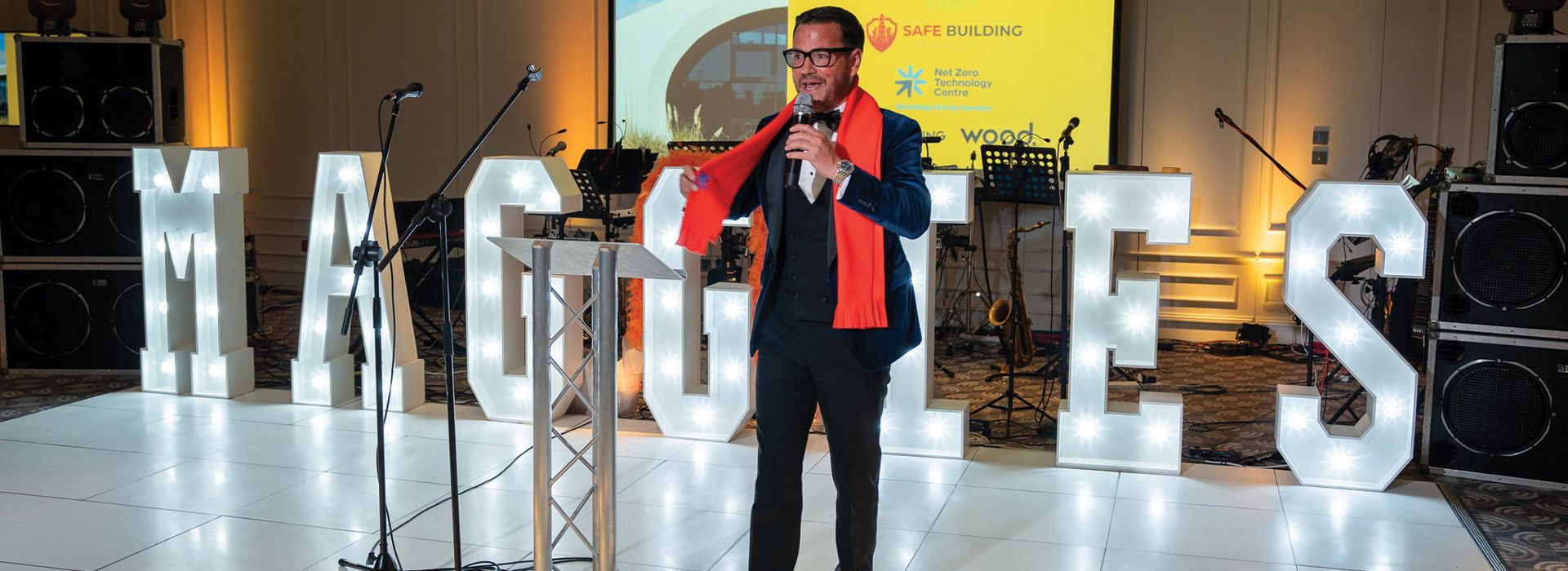 Man in orange scarf standing near large Maggie's letters in lights hosting an event