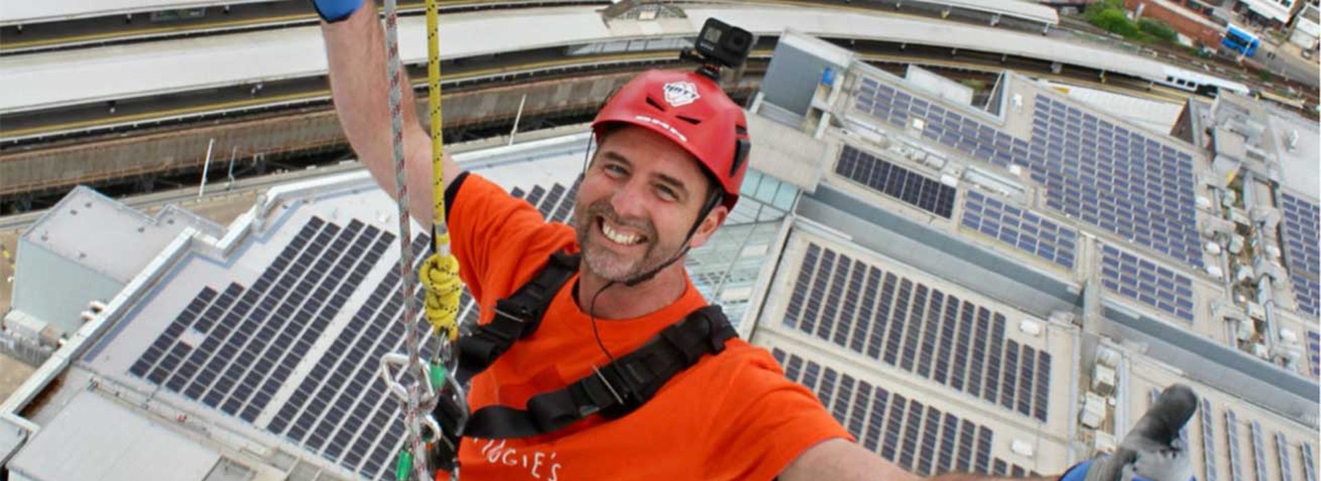 Man smiling and abseiling Spinnaker tower in Maggie's orange t-shirt