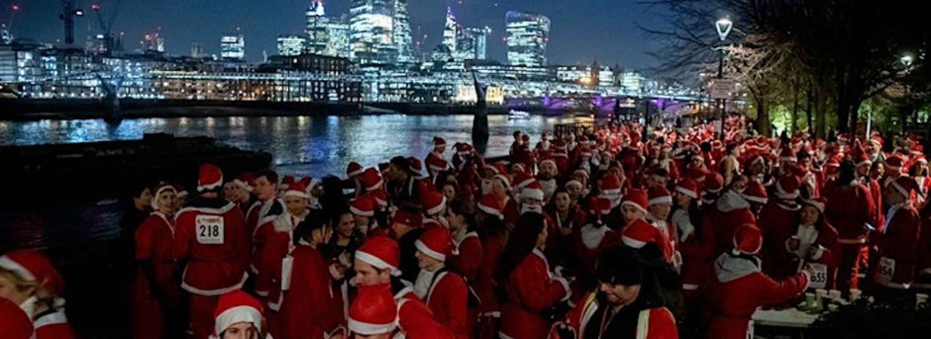 Panorama shot of hundreds of people dressed as Santa with a late night cityscape in the background