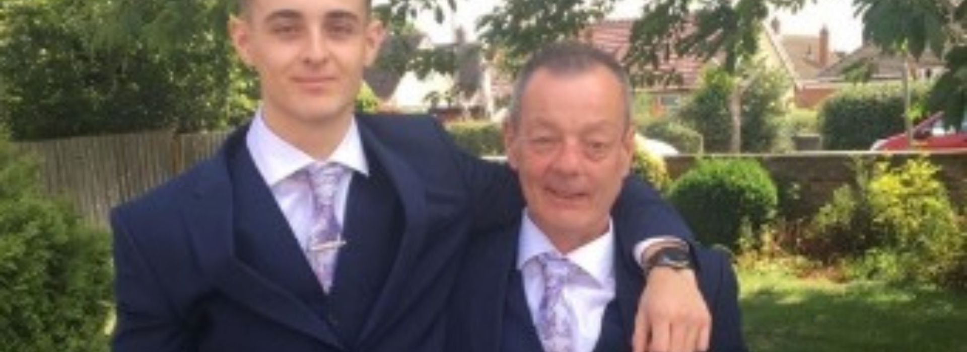 Patrick and his son wearing suits smiling and hugging