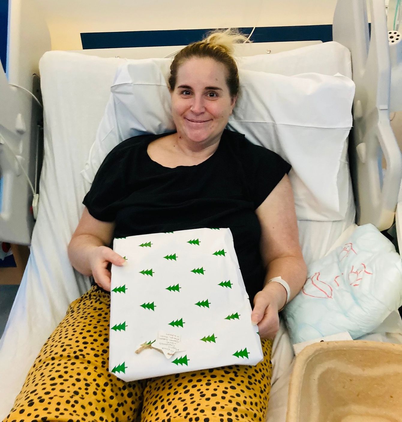 Gemma smiling and holding Christmas present from hospital bed