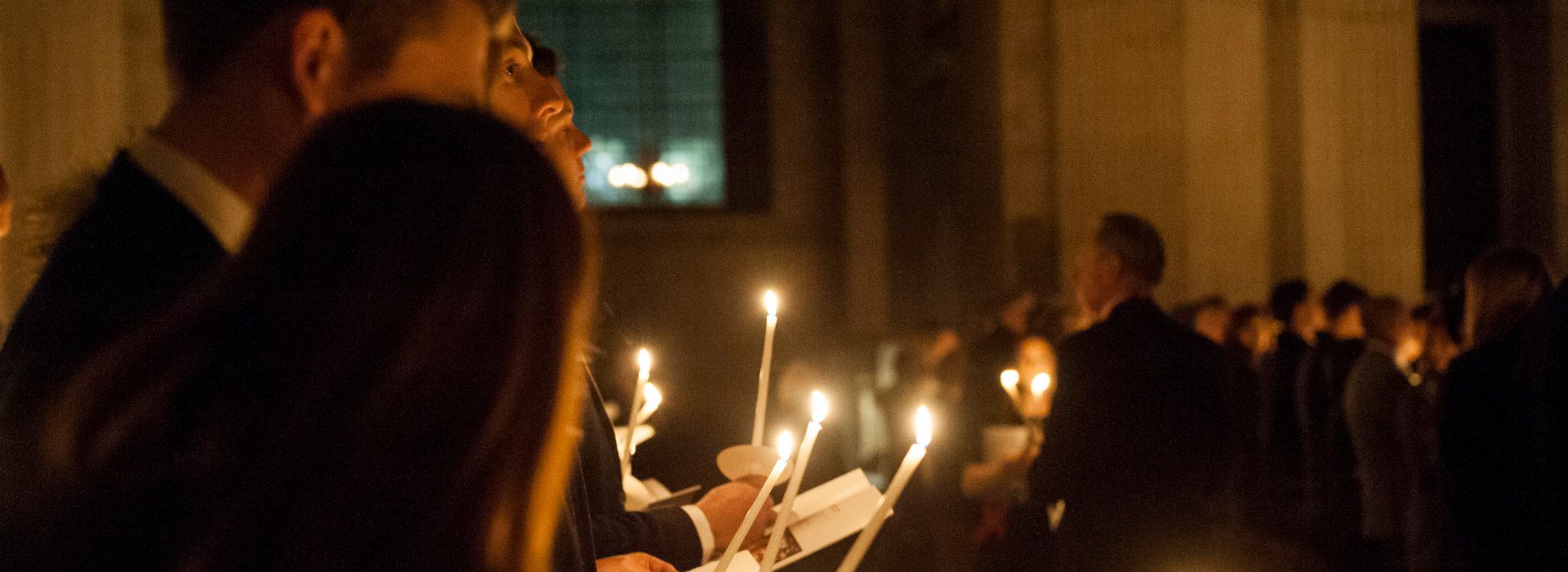 Rows of people singing hymns by candlelight in church