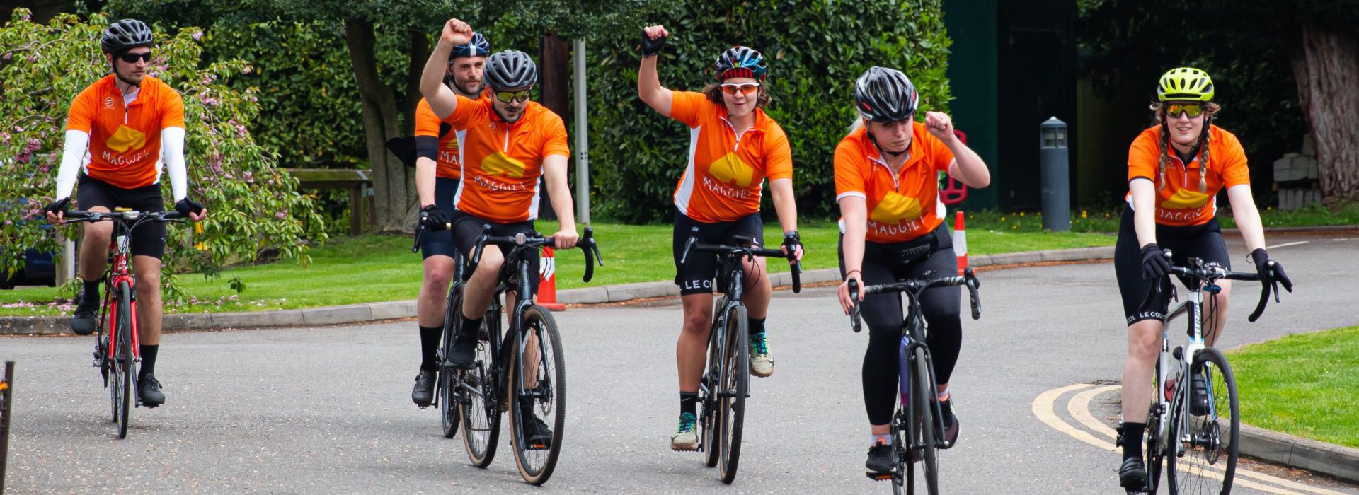 Group of cyclists in Maggie's jerseys cheerings on their bikes