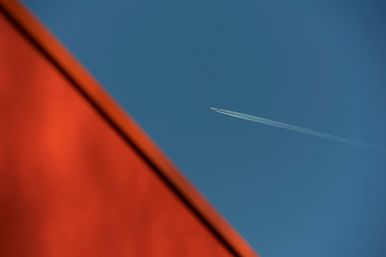 Abstract photo of orange roof of Maggie's West London and blue sky with plane flying over