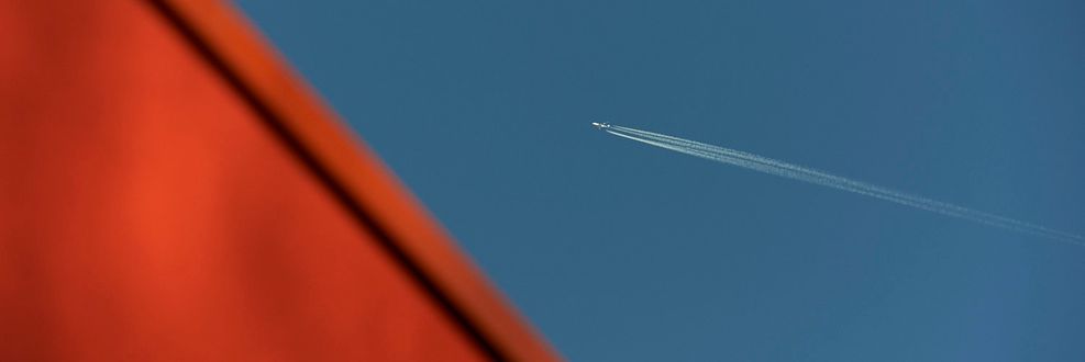 Abstract photo of orange roof of Maggie's West London and blue sky with plane flying over