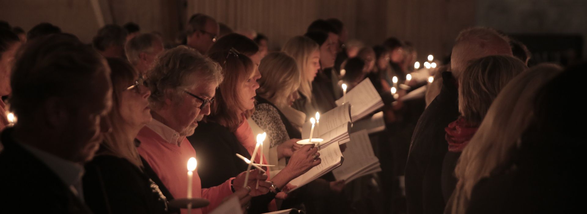 Congregation at Maggie's Carol Concert at St Paul's Cathedral in 2023, reading hymn booklets by candlelight