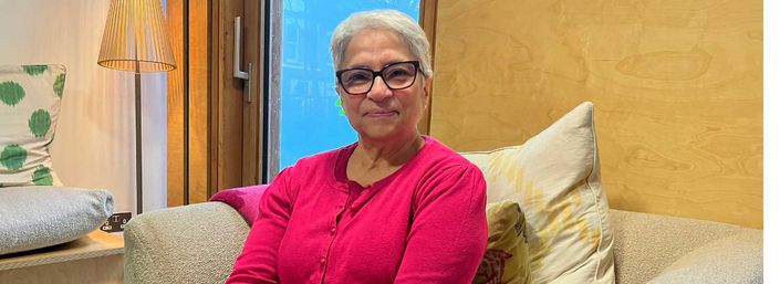 Khorshed wearing a bright pink cardigan sitting and smiling in our West London centre